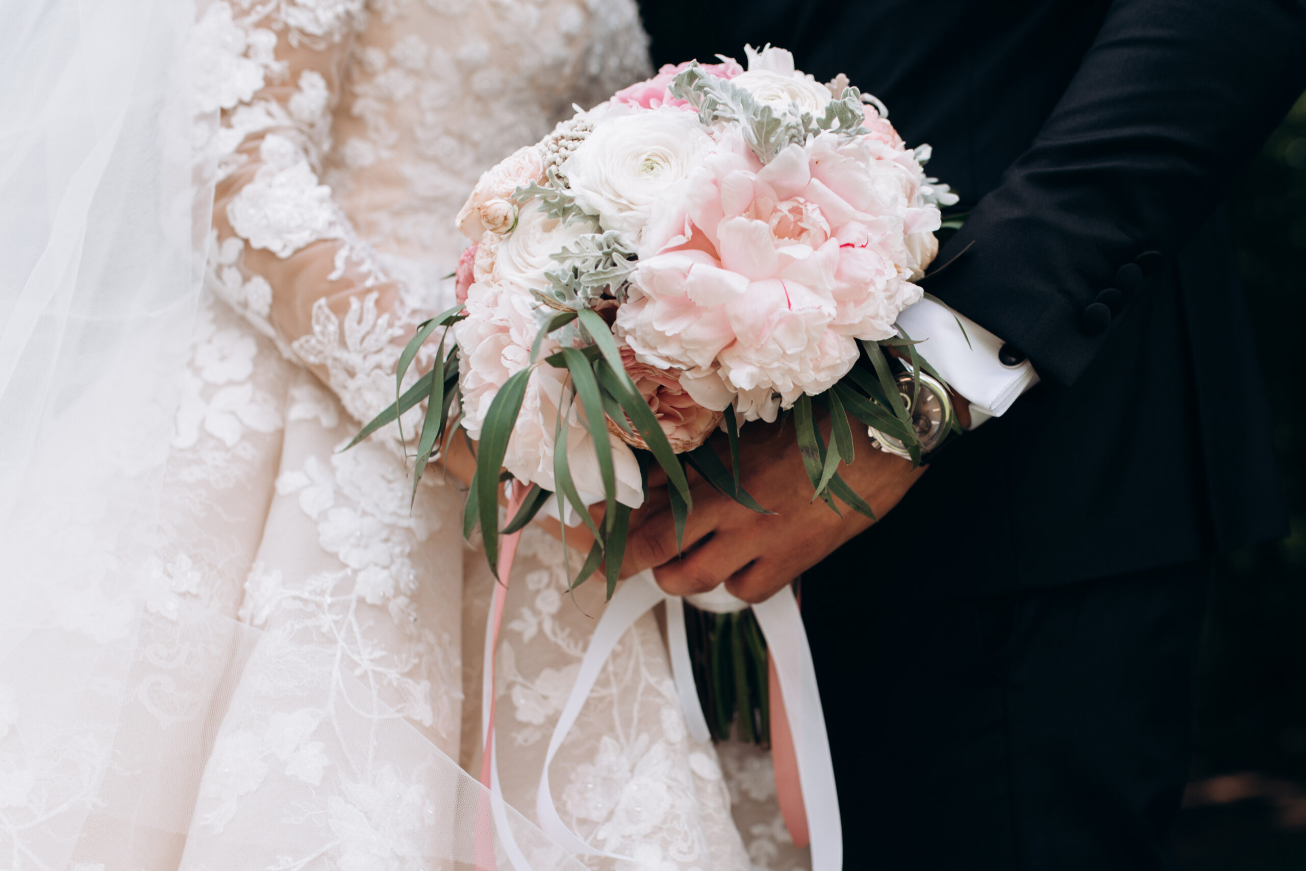 Frontview of groom and brides hands together are holding wedding pink bouquet